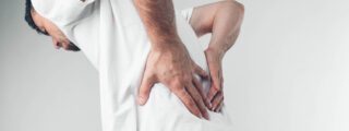 Mężczyzna trzymający się za plecy z bólem pleców, na białym tle. Objawy bólu kręgosłupa, zesztywniające zapalenie stawów kręgosłupa (ZZSK).