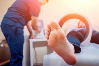 Pacjent leżący na stole do terapii, z nogą umieszczoną w polu magnetycznym podczas zabiegu rehabilitacyjnego.