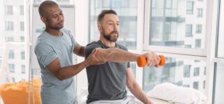 Fizjoterapeuta pomagający pacjentowi podnieść rękę z ciężarkiem, wspierając trening funkcjonalny.